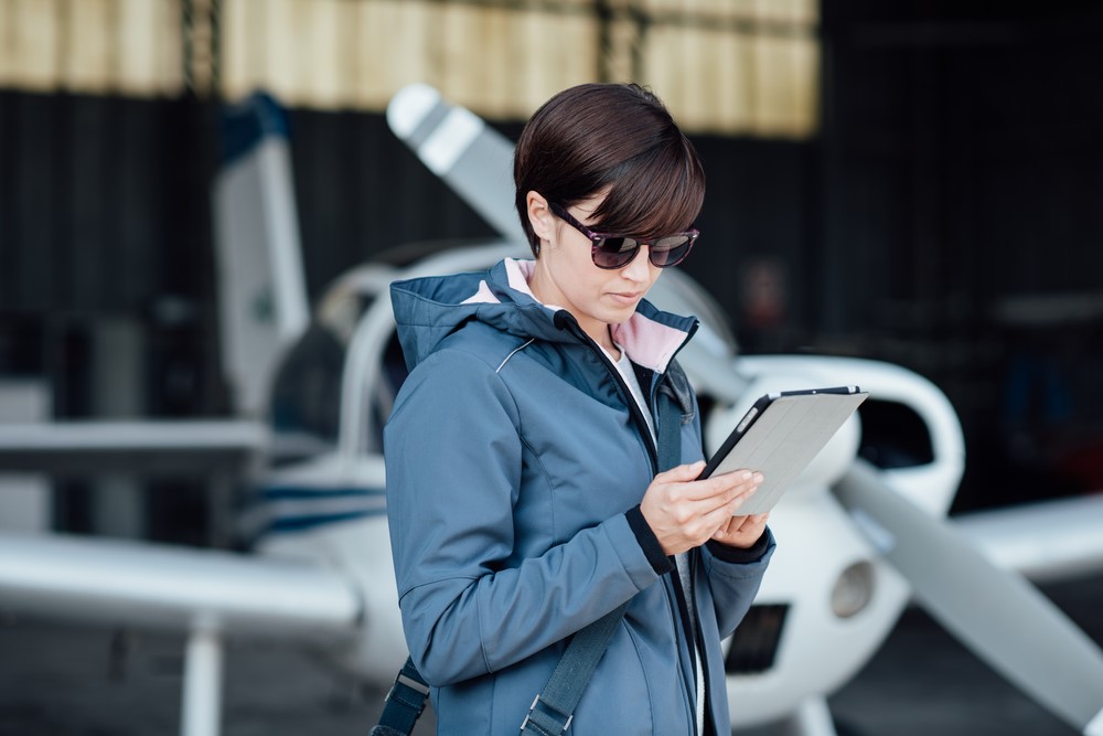 A woman in sunglasses checks her phone near a small aircraft. A woman in sunglasses checks her phone near a small aircraft.